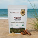 AyuMantra Arjuna Powder packaging on a beach with ocean view
