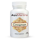 A bottle of AyuMantra brand Cinnamon capsules with 60 capsules inside. The label is white with a gold and red floral design and text.