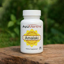 AyuMantra Amalaki dietary supplement bottle on a wooden surface with a green blurred background.