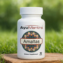 AyuMantra Amaltas dietary supplement bottle on a wooden surface with a green grass background.