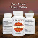 Three bottles of AyuMantra Ashoka Ghan dietary supplements on a blurred natural background.