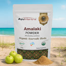 AyuMantra Amalaki Powder packaging with green fruits and powder on a beach background