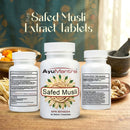 Three white supplement bottles labeled AyuMantra Safed Musli are arranged on a wooden surface with herbal ingredients and a mortar-and-pestle in the background. The center bottle shows the front label, while the side bottles show the back product information panels.