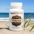 AyuMantra Vijaysar dietary supplement bottle on a sandy beach with ocean view