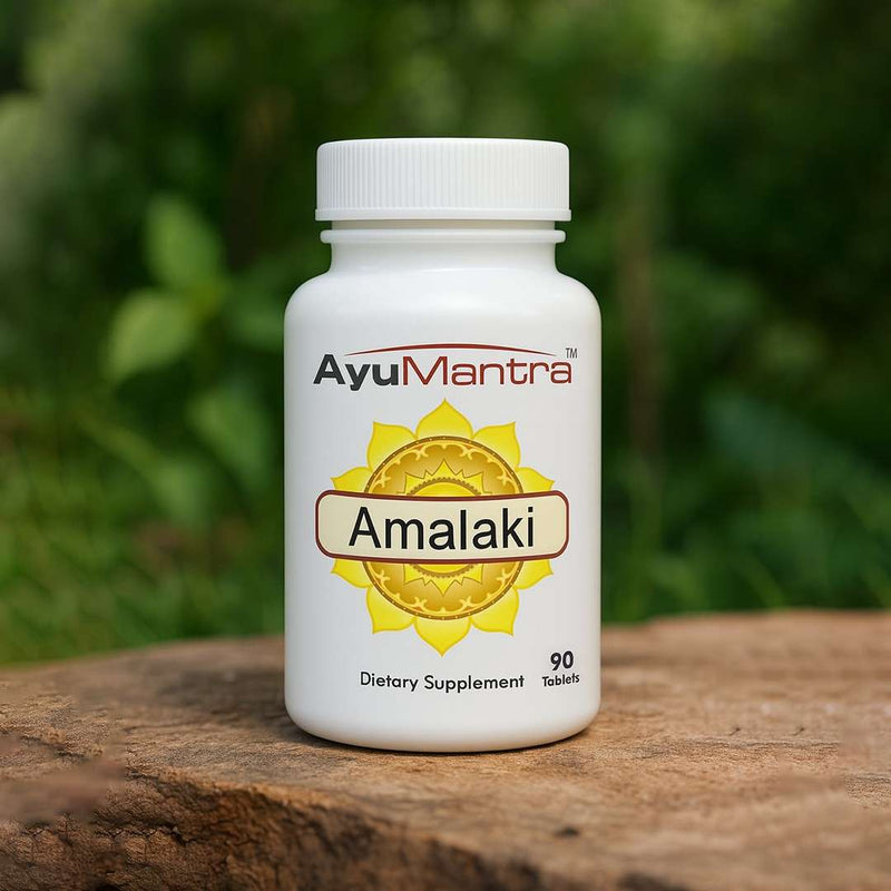 AyuMantra Amalaki dietary supplement bottle on a wooden surface with a green blurred background.