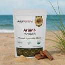 AyuMantra Arjuna Powder packaging on a beach with ocean view
