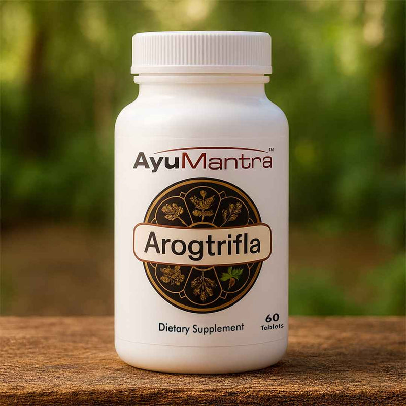 AyuMantra Arogtrifla dietary supplement bottle on a wooden surface with a blurred natural background. 
