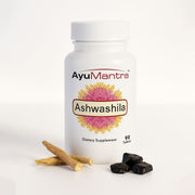 Ashwashila tablets bottle with ashwagandha roots and shilajit pieces on clean white background.