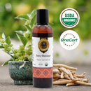 Baby massage oil bottle with USDA Organic and OneCert Organic logos, surrounded by greenery and roots.