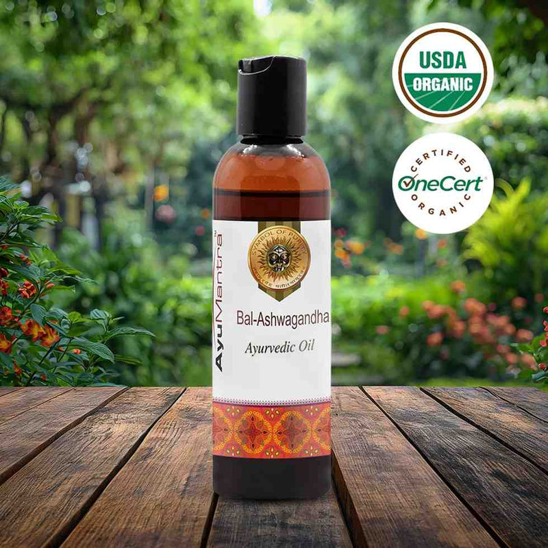 Bottle of Bal Ashwagandha Ayurvedic Oil with USDA Organic and OneCert Organic logos on a wooden surface with a garden background.