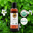 Brahmi organic ayurvedic oil bottle with USDA Organic and oneCert Organic logos on a green leafy background.
