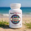 AyuMantra Brahmi dietary supplement bottle on a sandy beach with ocean in the background.