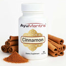 AyuMantra cinnamon capsules bottle with cinnamon sticks and powder on a white background.