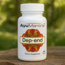 AyuMantra Dep-end dietary supplement bottle on a wooden surface with a blurred green background. 