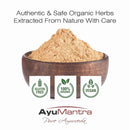Wooden bowl filled with brown powder labeled 'AyuMantra Pure Ayurveda' with organic certification logos.