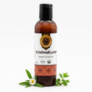 Ayumantra Krishna Kuntal Oil bottle on white background with bhringraj and herbal leaves beside it