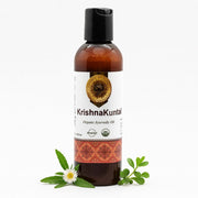 Ayumantra Krishna Kuntal Oil bottle on white background with bhringraj and herbal leaves beside it