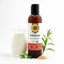 Ayumantra Ksheerbala Oil bottle with milk jug, sesame seeds and herbs on a clean white background.