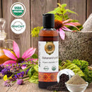 Bottle of Ayurvedic oil with organic certification logos, flowers, and herbs on a wooden background
