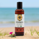 Bottle of Mahavishgarbha Organic Ayurvedic Oil on a sandy beach with ocean in the background
