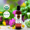 Bottle of Mahavishgarbha Organic Ayurvedic Oil with USDA Organic and OneCert logos on a floral background.