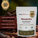 AyuMantra Manjistha Powder packaging with product details and branding on a dark background.