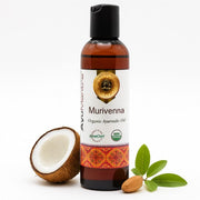 Bottle of Murivenna organic ayurvedic oil with a coconut, almond, and leaves on a white background
