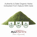 Pile of green herbs with AyuMantra branding and certification logos on a white background