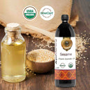 Bottle of AyuMandira Sesame Organic Ayurvedic Oil with a corked glass bottle and sesame seeds on a wooden background.