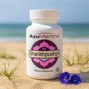 AyuMantra Shankhpushpi dietary supplement bottle on a sandy beach with ocean view