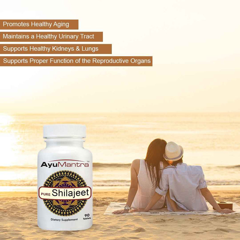 AyuMantra Shilajit pills bottle on beach near relaxing couple at sunset, Ayurvedic vitality supplement
