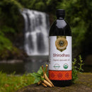 Bottle of Shirodhara organic ayurvedic oil with a natural background featuring a waterfall.
