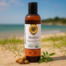 Bottle of Shoolhar Organic Ayurvedic Oil on a sandy beach with ocean view