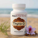 AyuMantra Thyro-D tablets bottle on a sandy beach with flower and sea in the background.