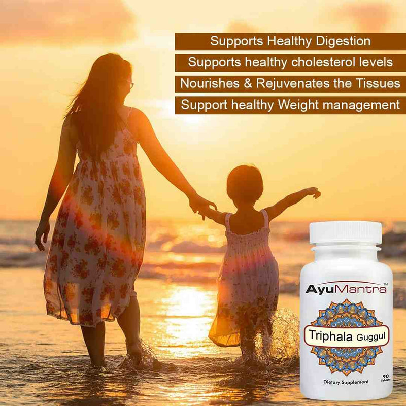 AyuMantra Triphala Guggul tablets bottle beside a mother and child walking on the beach at sunset.
