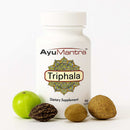 AyuMantra Triphala tablets bottle on white background with whole Triphala fruits around it.