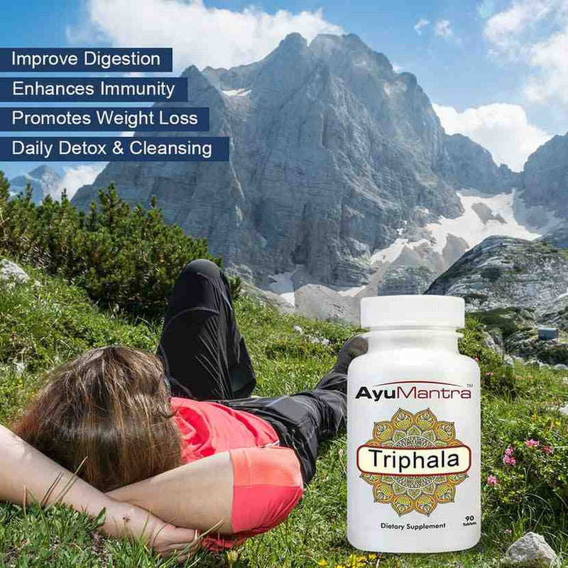 Lifestyle photo of AyuMantra Triphala tablets beside a relaxed person in a mountain landscape