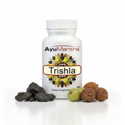 AyuMantra Trishala tablets bottle with Triphala fruits and Shilajeet pieces on a white background.