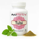 AyuMantra Tulsi holy basil tablets bottle on white background with green leaves and herb powder.