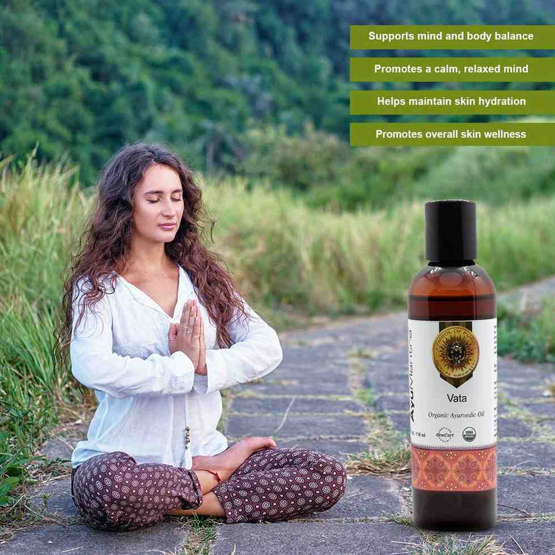 Woman meditating outdoors with a bottle of Vata organic ayurvedic oil.
