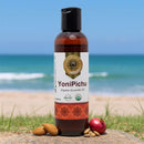 YoniPichu organic ayurvedic oil bottle with almonds and a pomegranate on a beach background