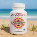 AyuMantra Chandraprabha vati tablets bottle on beach sand with blue sea in the background.