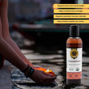 Bottle of Dhaawantharam Organic Ayurvedic Oil with text highlighting benefits, blurred background of person with lit candle.