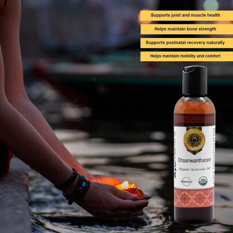 Bottle of Dhaawantharam Organic Ayurvedic Oil with text highlighting benefits, blurred background of person with lit candle.