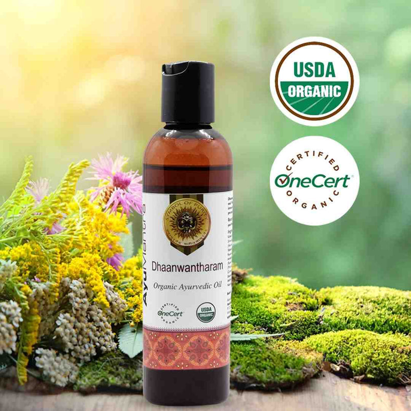 Bottle of Dhaanwantharam Organic Ayurvedic Oil with USDA Organic and OneCert logos on a natural background.