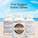 AyuMantra Guggulu tablets in front and back bottles with supplement facts and pure extract text on a beach backdrop.