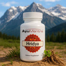 Ayumantra Hridya tablets bottle standing on soil with green grass and snowy mountains behind it